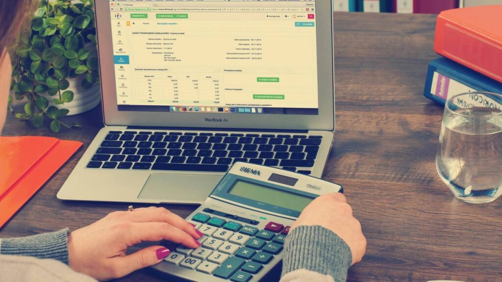 A photo of a woman using a calculator in front of her laptop